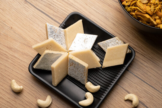 Diamond-shaped Kaju Katli slices arranged with almonds on a festive tray.