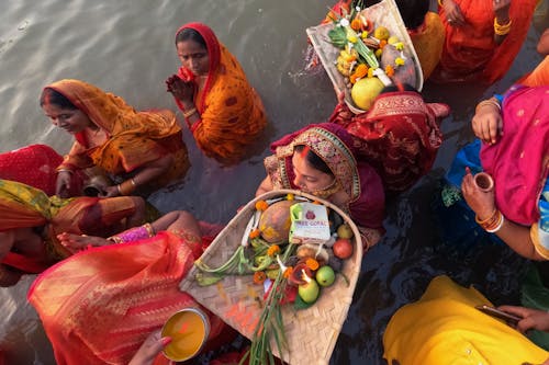 Women in vibrant sarees performing evening rituals on the riverbank.